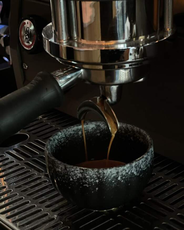 Espresso pulling from the portafilter into a black cup